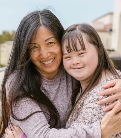 A joyful moment of a mother and daughter with Down syndrome sharing a warm embrace outdoors.